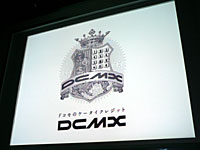 「貨幣」「電話のボタン」「世界地図」「王冠（信頼のシンボル）」が電話機をモチーフにした“盾”の上にあしらわれた「DCMX」の紋章